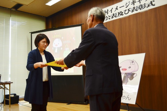 「しみちゃん」をデザインした高松絵美さん 松本村長より表彰状と盾が贈られました。